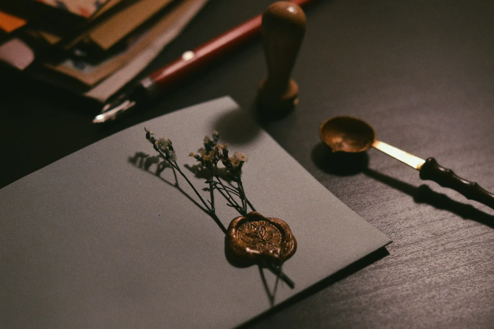 A bronze wax seal pressed onto gray card beside a wooden seal stamp and a wax spoon