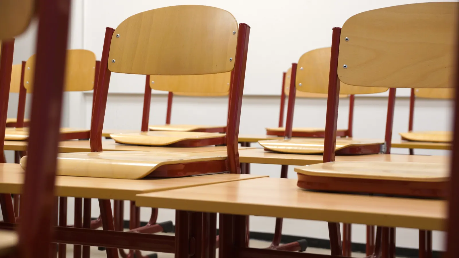 Rows of wooden classroom chairs on desks in a tidy classroom