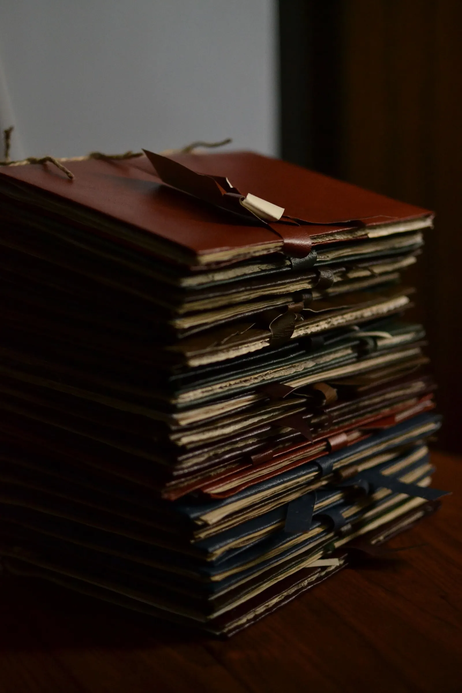 A tall stack of leather-bound folders and files tied with cord on a dark wooden table