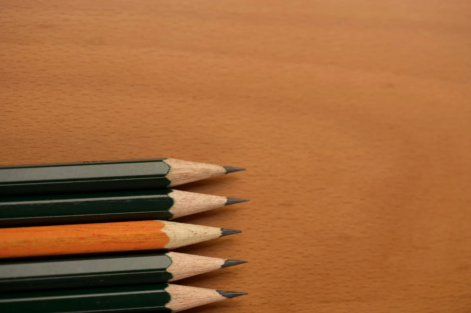 Five freshly sharpened pencils lined up on a warm wooden desk