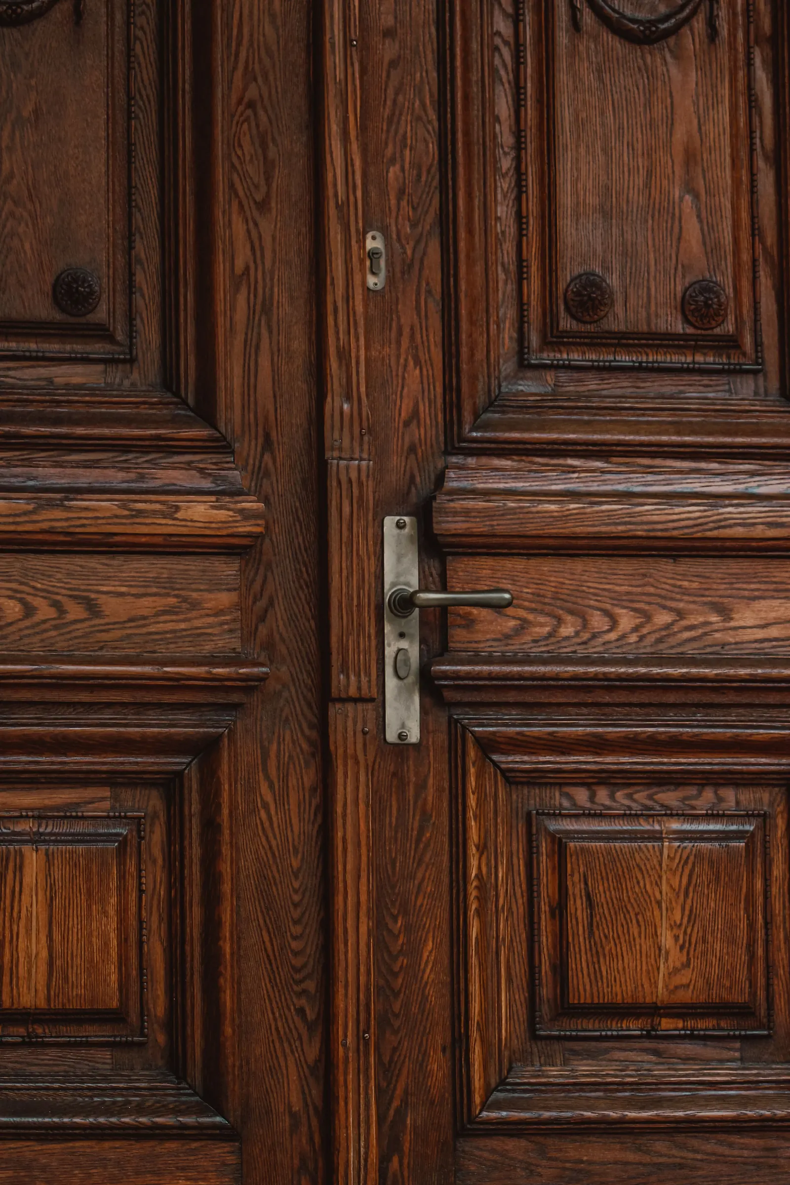 Heavy carved wooden double doors with a brass handle and lock