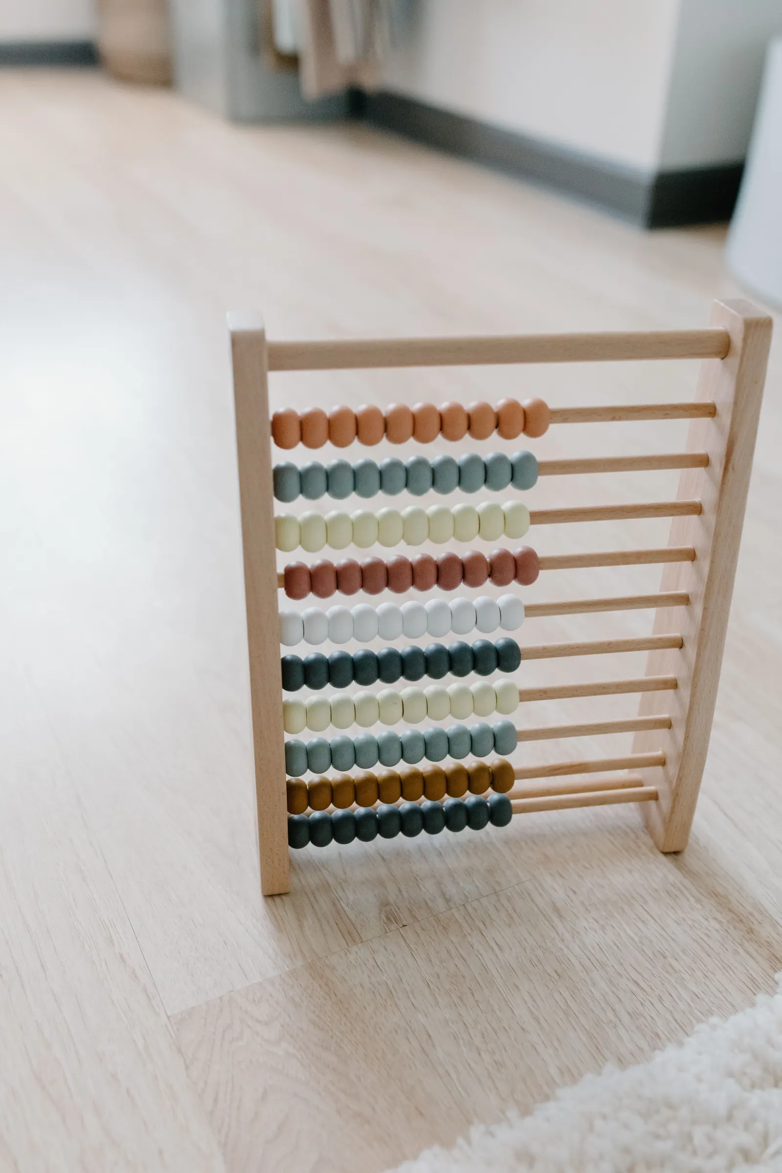 A wooden abacus with rows of muted colored beads standing on a pale oak floor