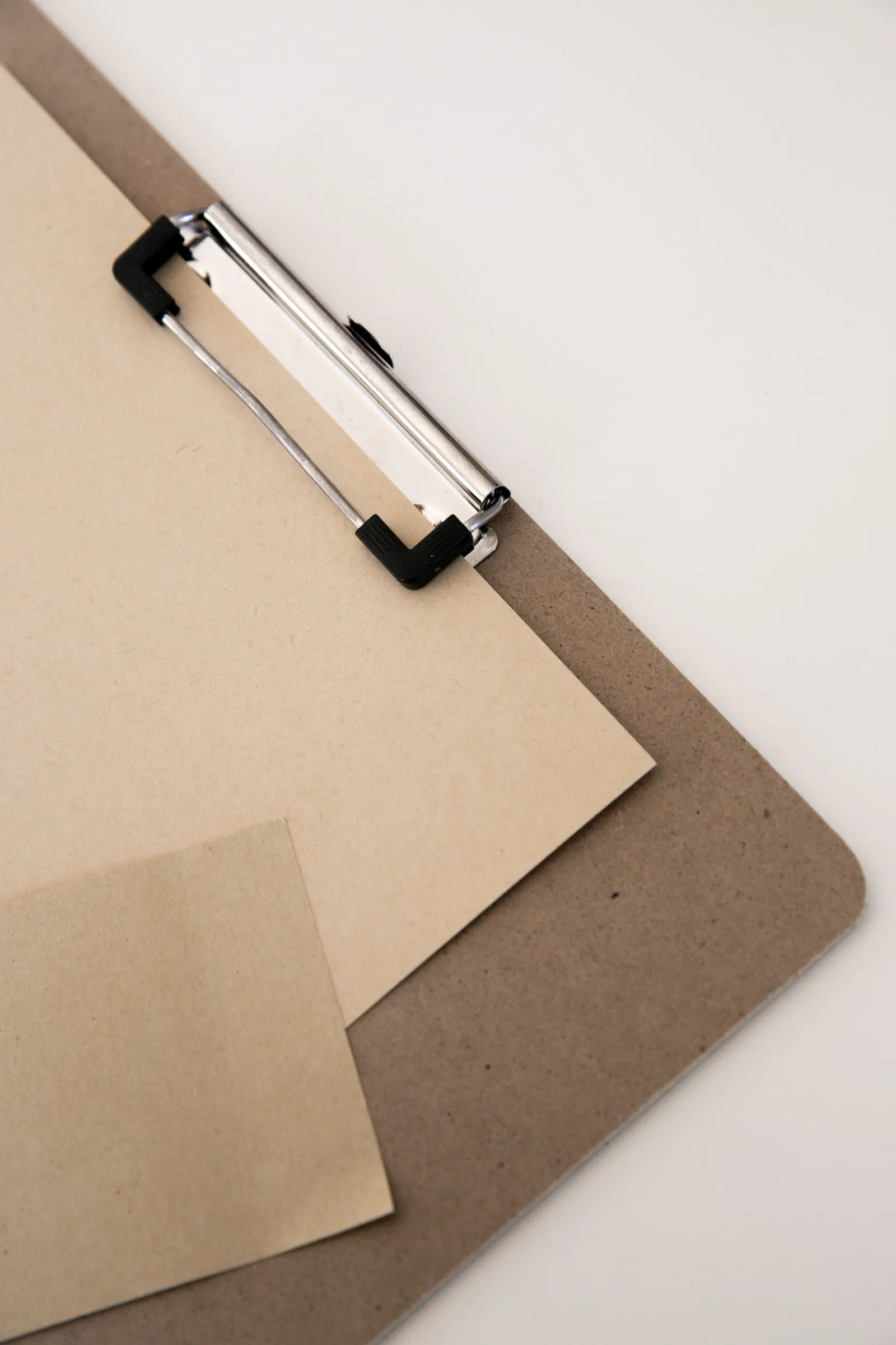 A kraft clipboard with a blank sheet lies on a white desk