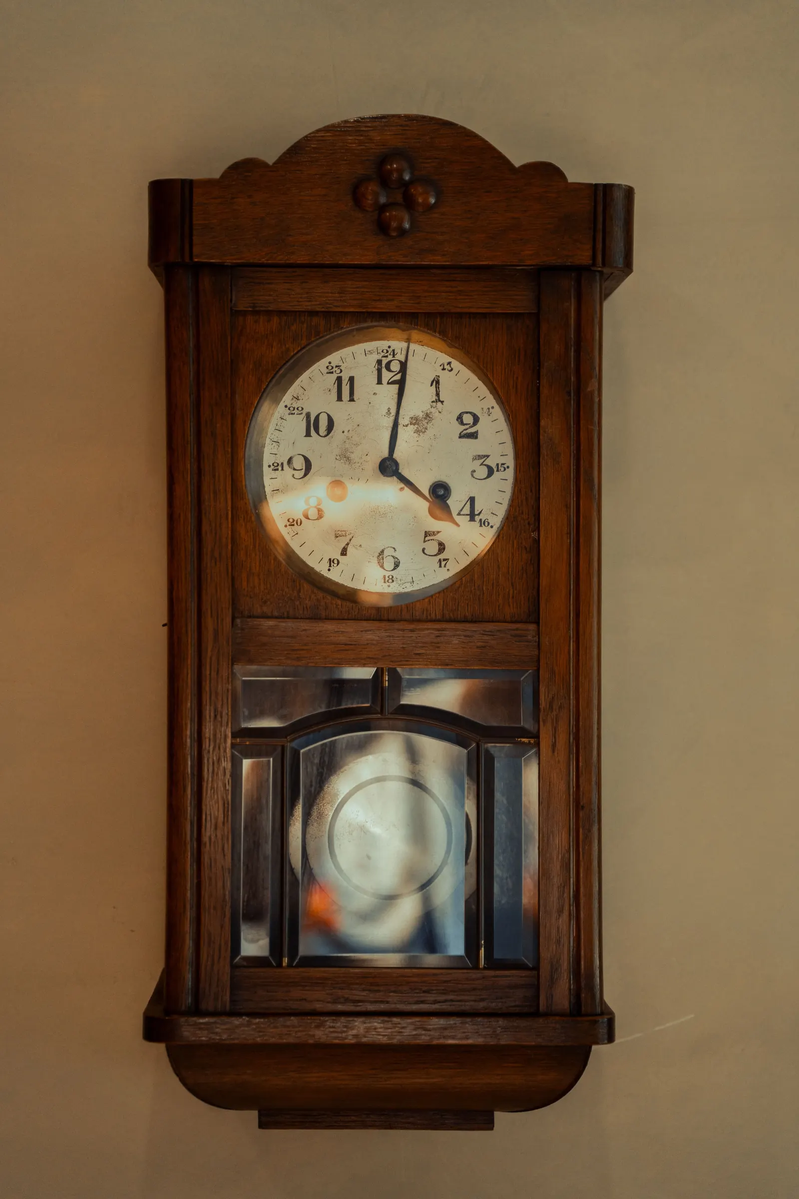 An old wooden wall clock with a round white face and a glass-fronted pendulum case