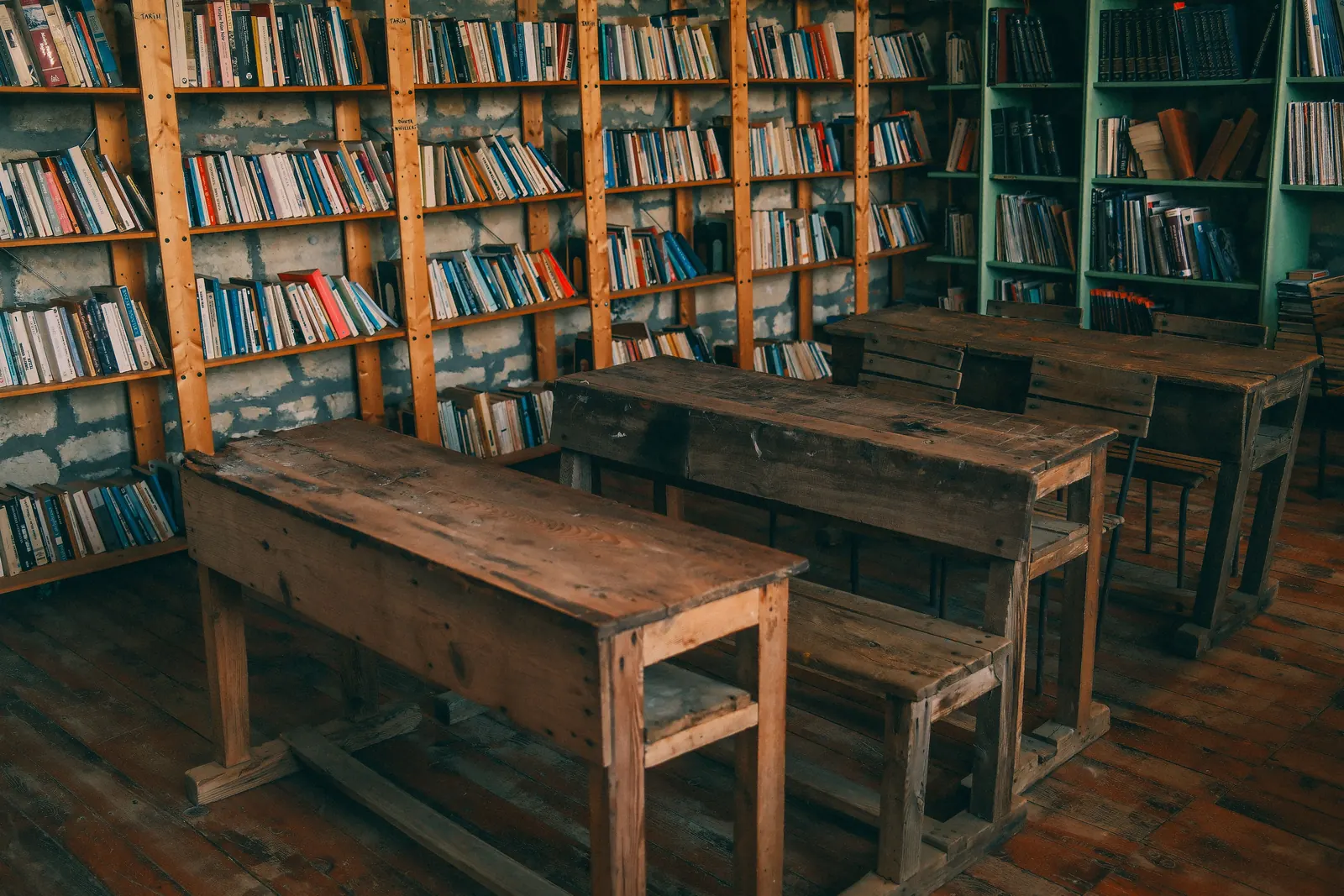Rows of old wooden school desks in a classroom lined with bookshelves