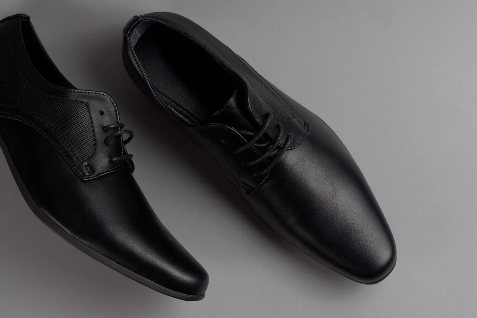 A pair of plain black lace-up leather shoes on a grey background