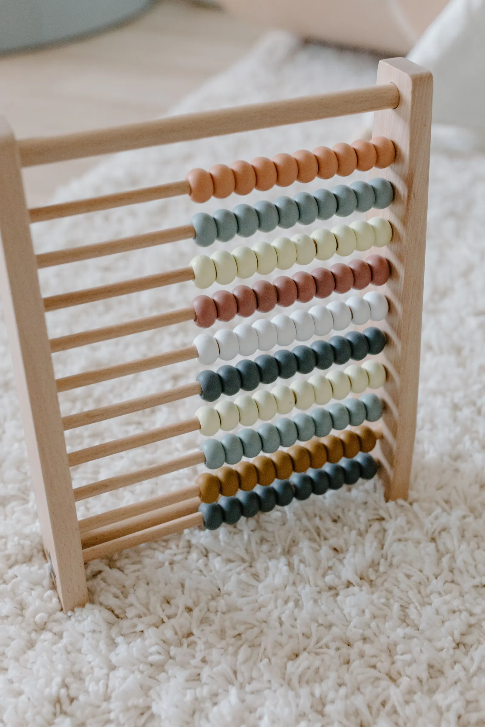A wooden abacus with rows of muted colored beads on a cream rug