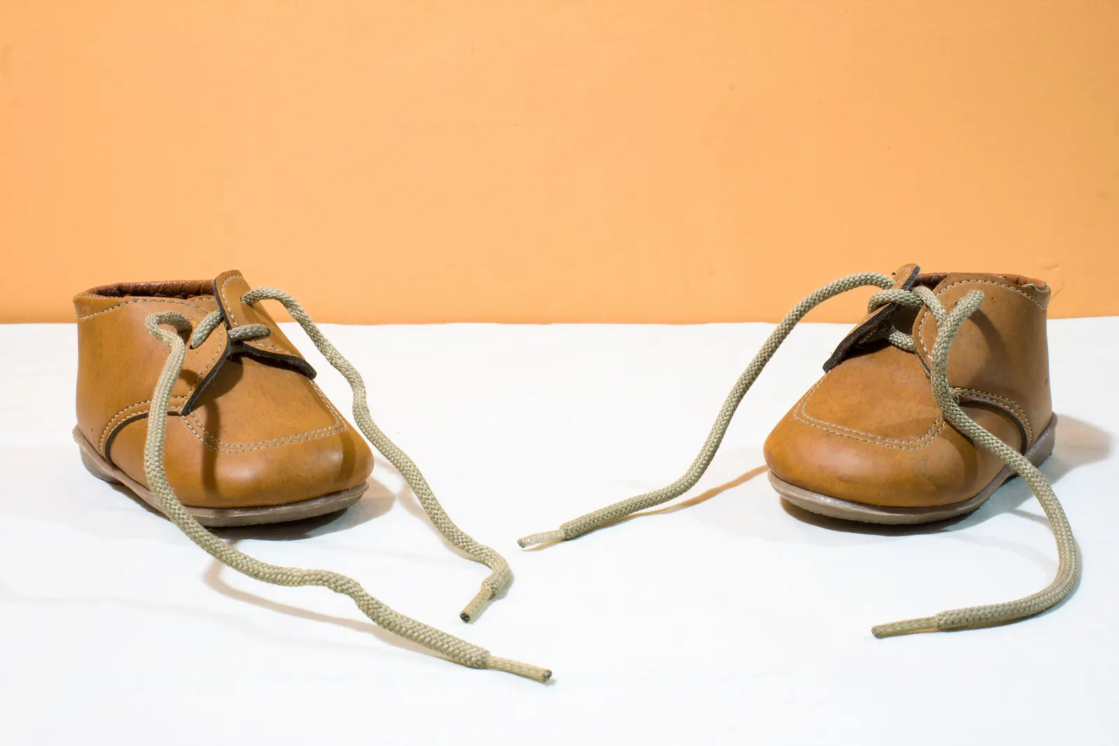 A pair of small tan leather children's shoes with loose laces on a white cloth