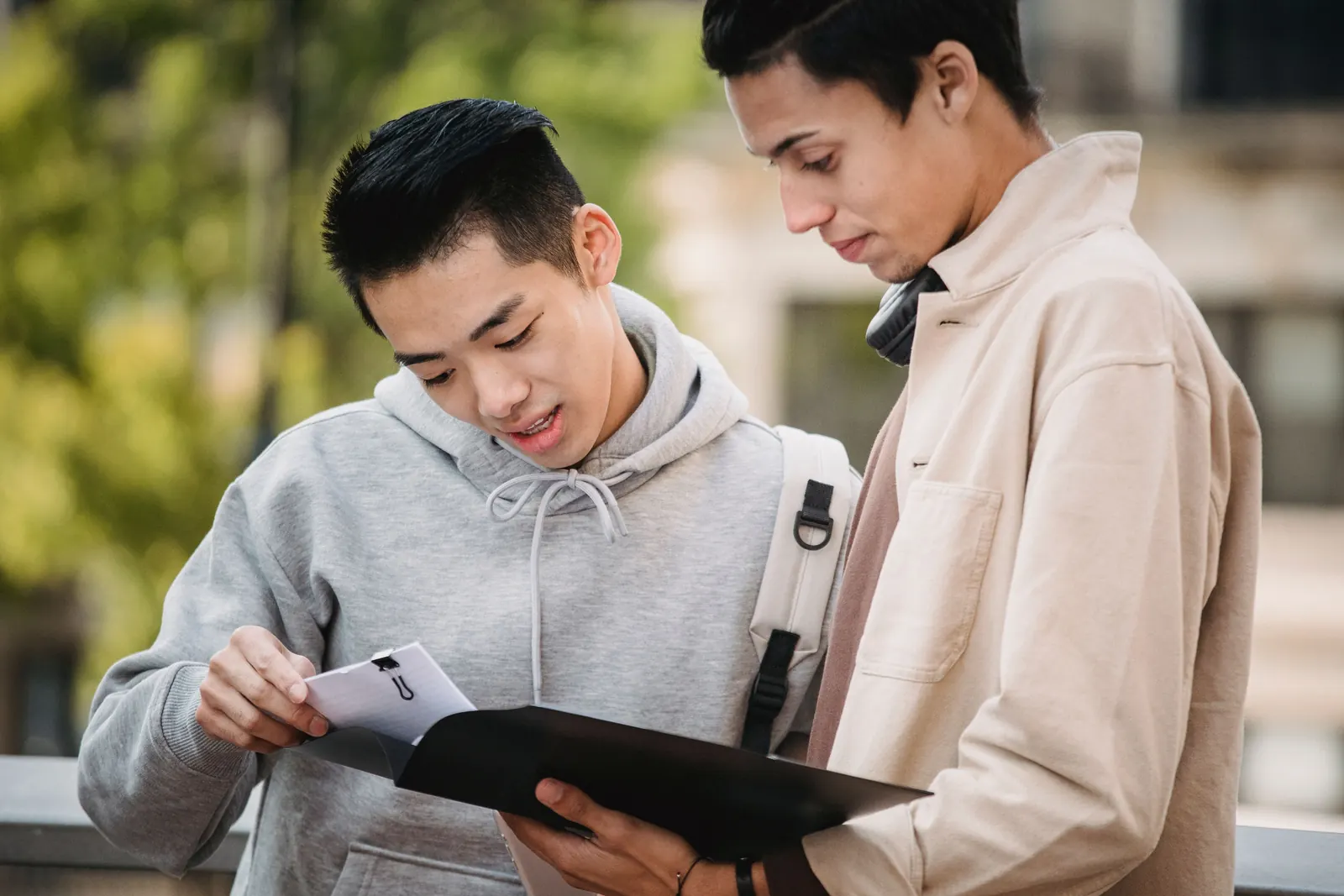 Two older teenage boys look over papers in a folder together outdoors
