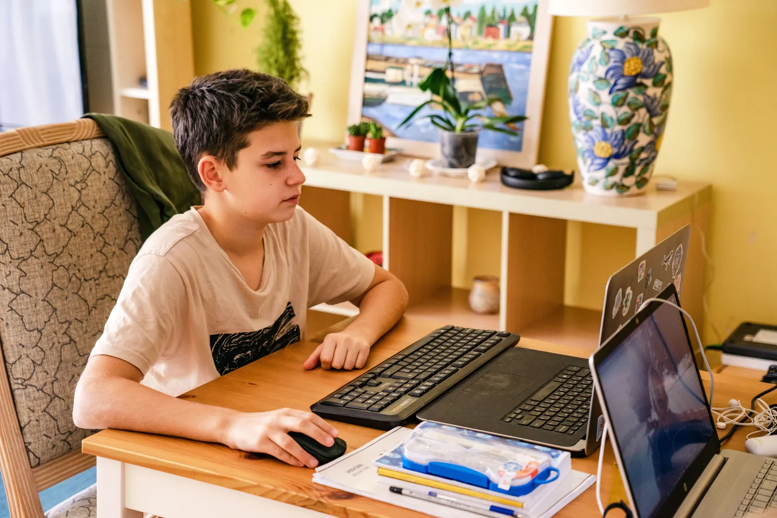 A teenage boy works at a computer with a keyboard and mouse at a home desk