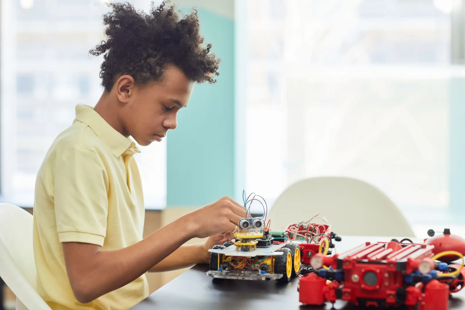 A boy in a yellow polo assembles a small robot car on a dark table