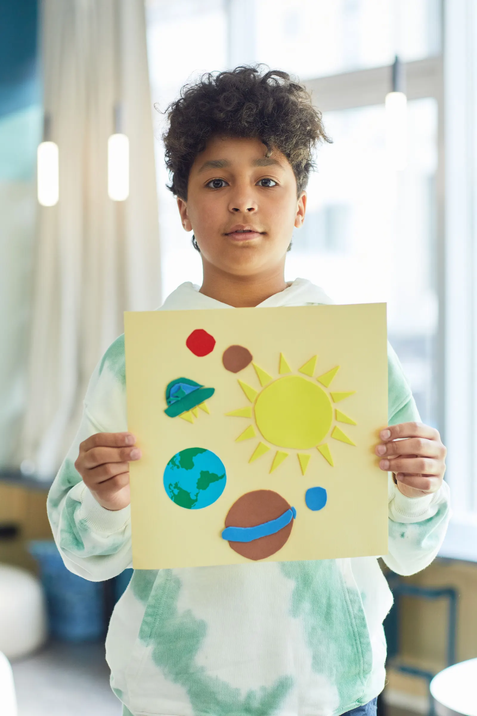 A teenage boy holds up a hand-made model of the solar system he has built