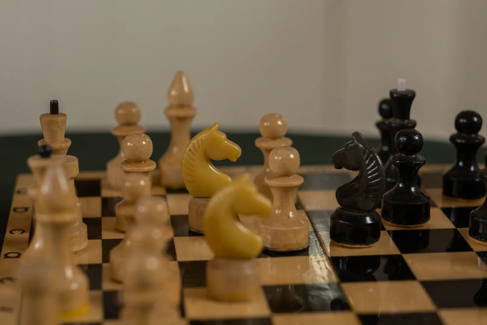 Wooden chess pieces mid-game on a black and cream board, a pale knight in the foreground