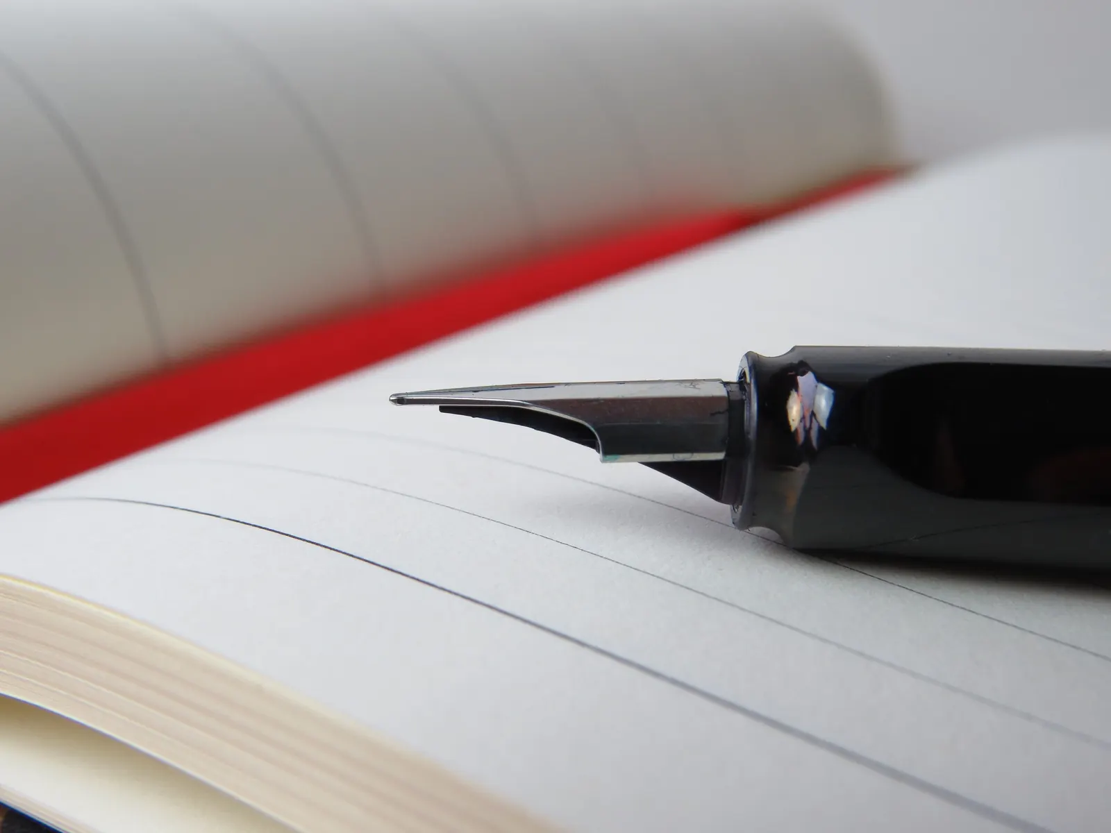 A black fountain pen resting on the lined pages of an open notebook with a red ribbon marker