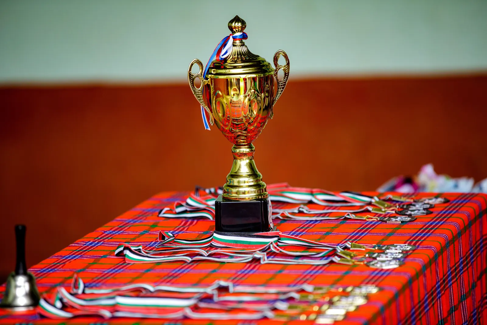 A gold trophy stands on a table laid with rows of medals on striped ribbons, ready for a prize-giving