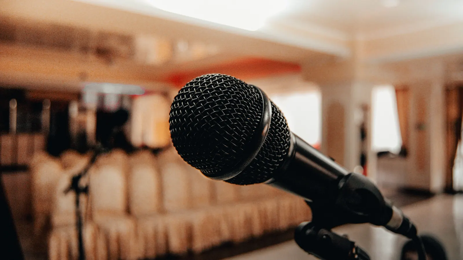 A microphone on a stand in front of rows of empty chairs in a bright hall