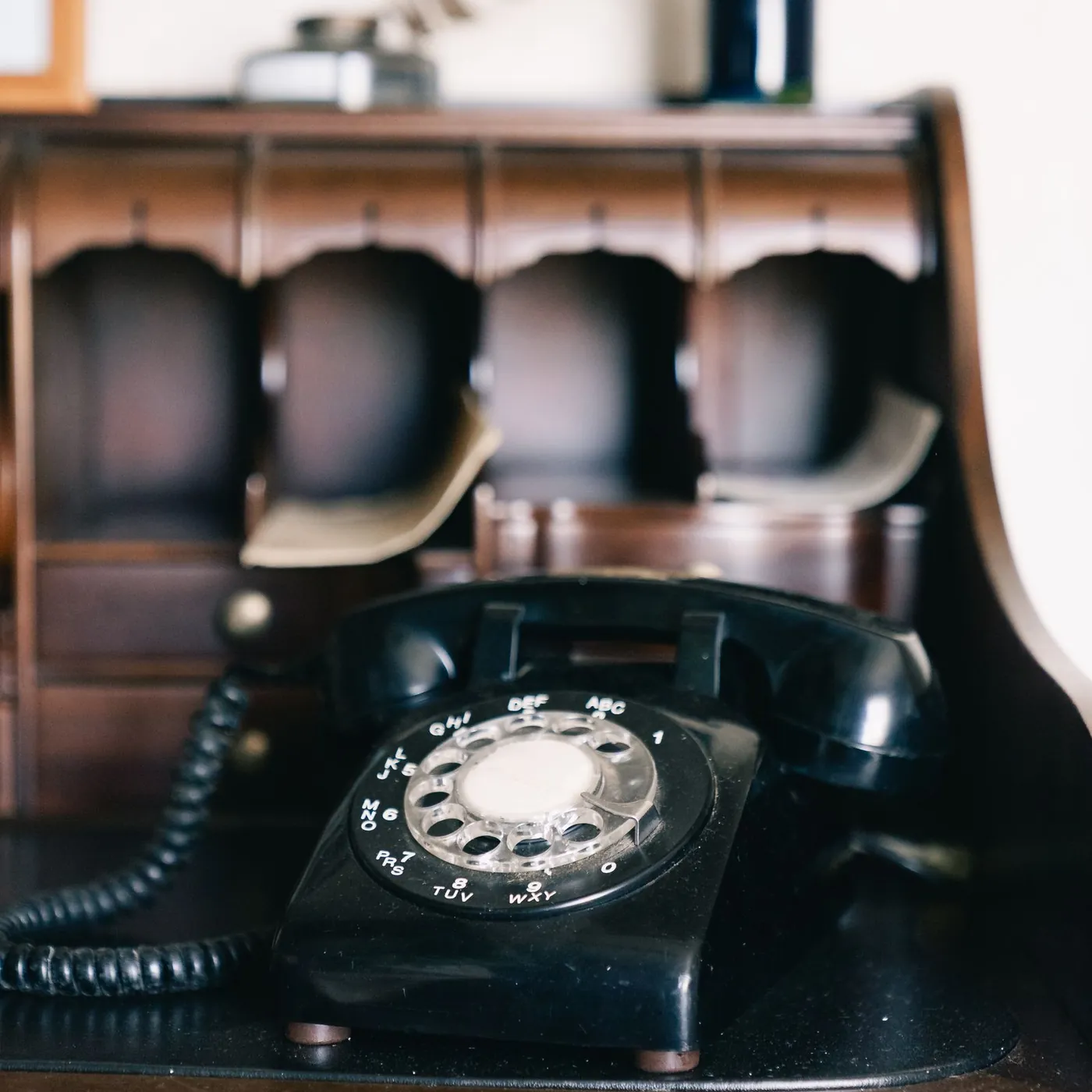 A black rotary desk telephone on a dark wooden secretary desk, with pigeonholes, a quill and an ink bottle behind