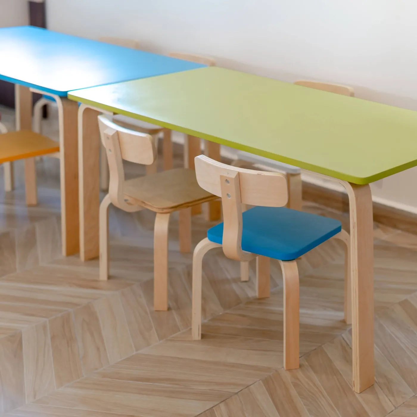 Rows of small bentwood children's chairs with colored seats tucked under low tables on a light herringbone wooden floor