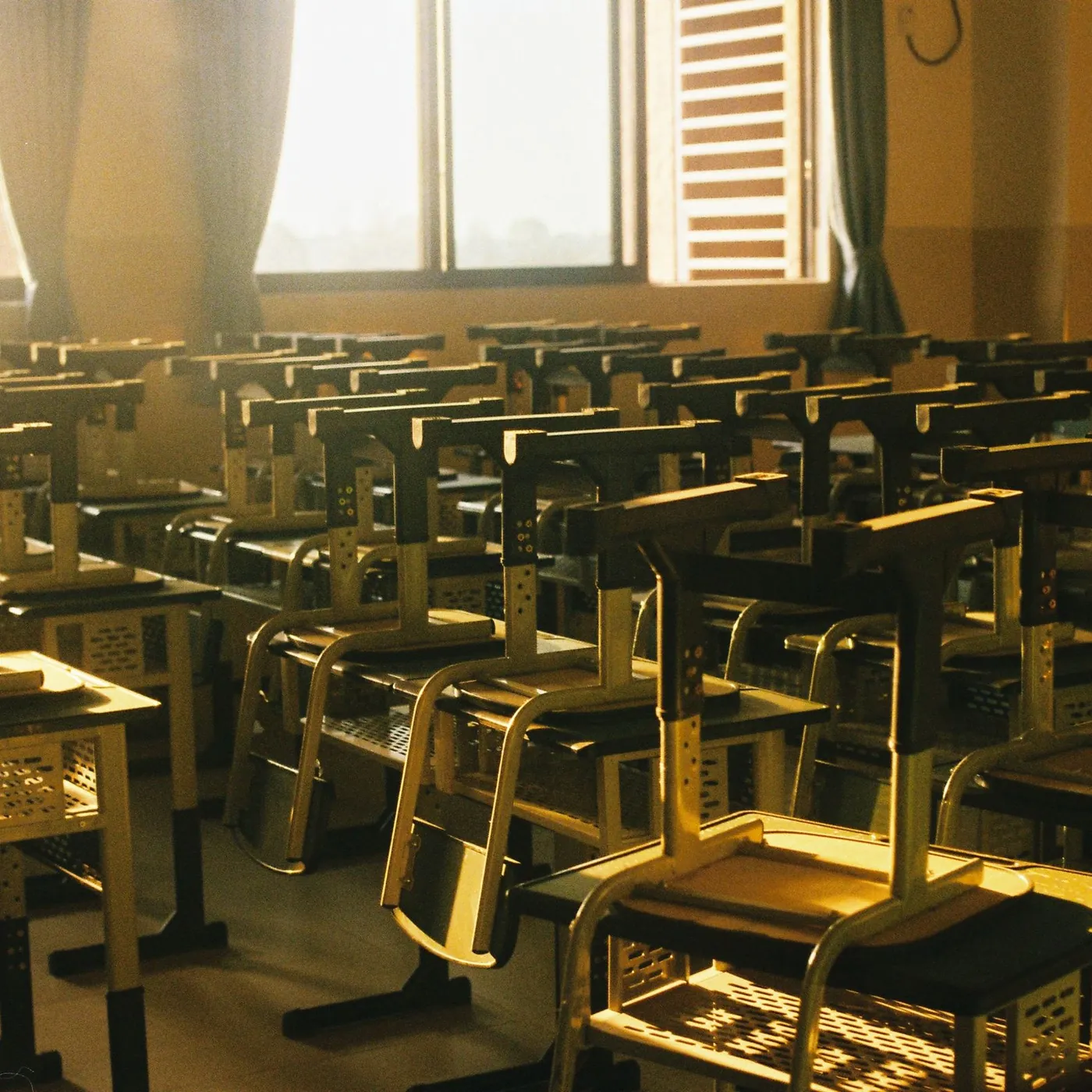An empty classroom at the end of the day, chairs upturned on rows of desks, lit gold by low sun through the windows