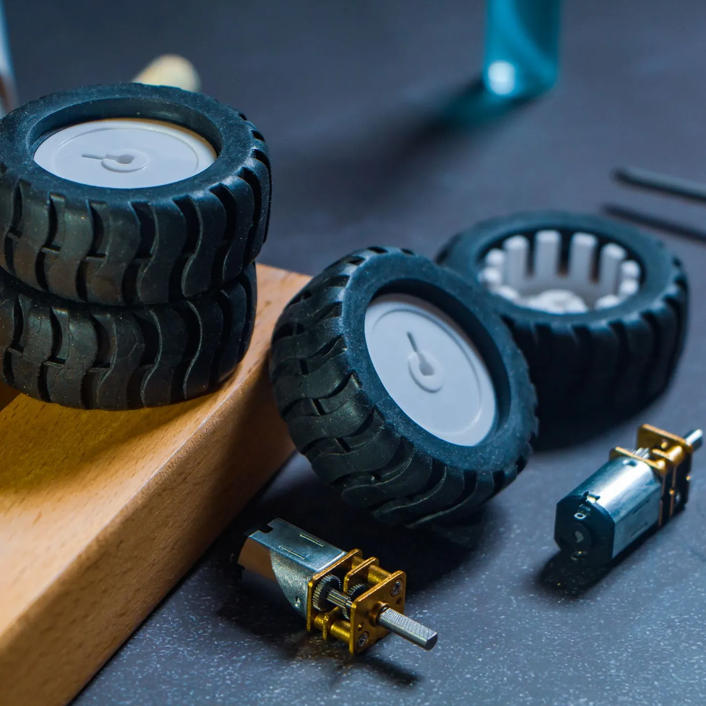 Small rubber robot wheels and two geared micro motors laid out on a wooden block and a dark workbench