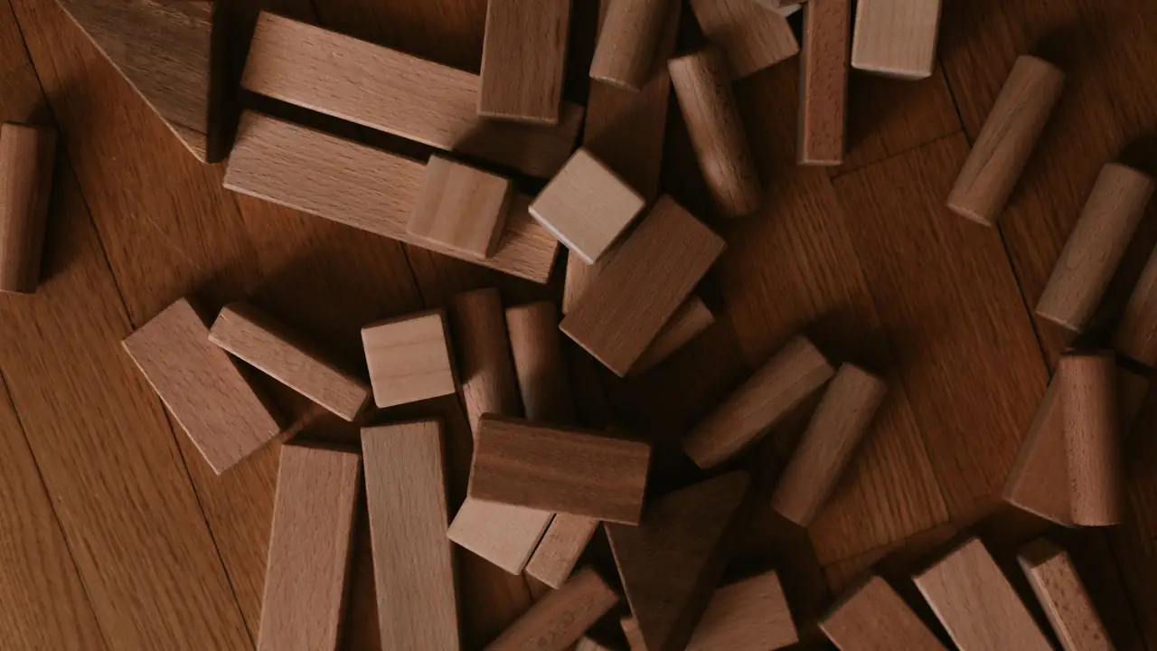 Plain beech building blocks scattered across a warm oak parquet floor, seen from above.