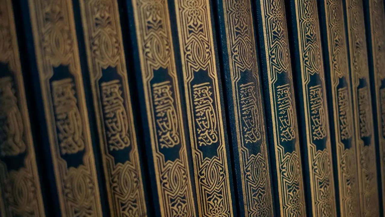 A shelf row of Qur'an volumes photographed close, gold-tooled spines on deep navy cloth.