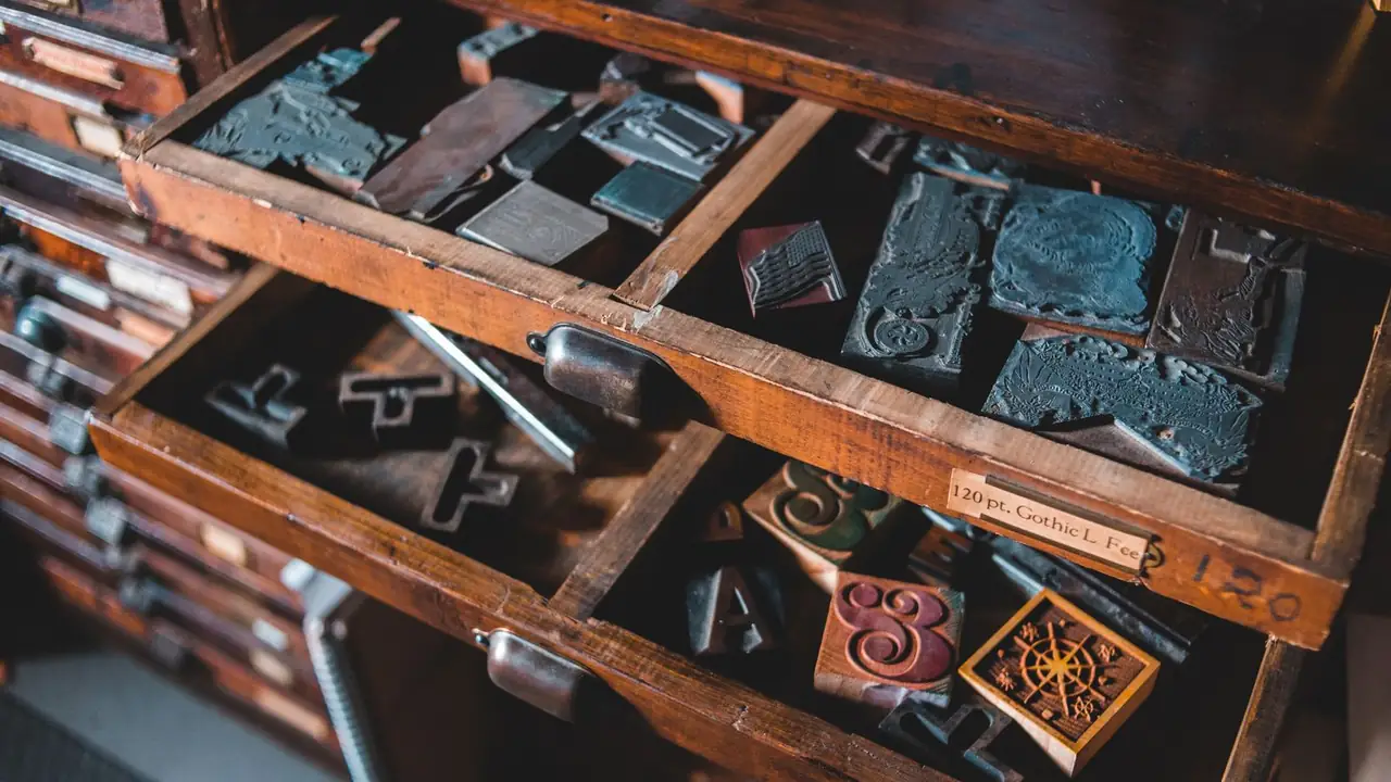 Two open drawers of a printer's type cabinet, holding metal cuts and wooden type.
