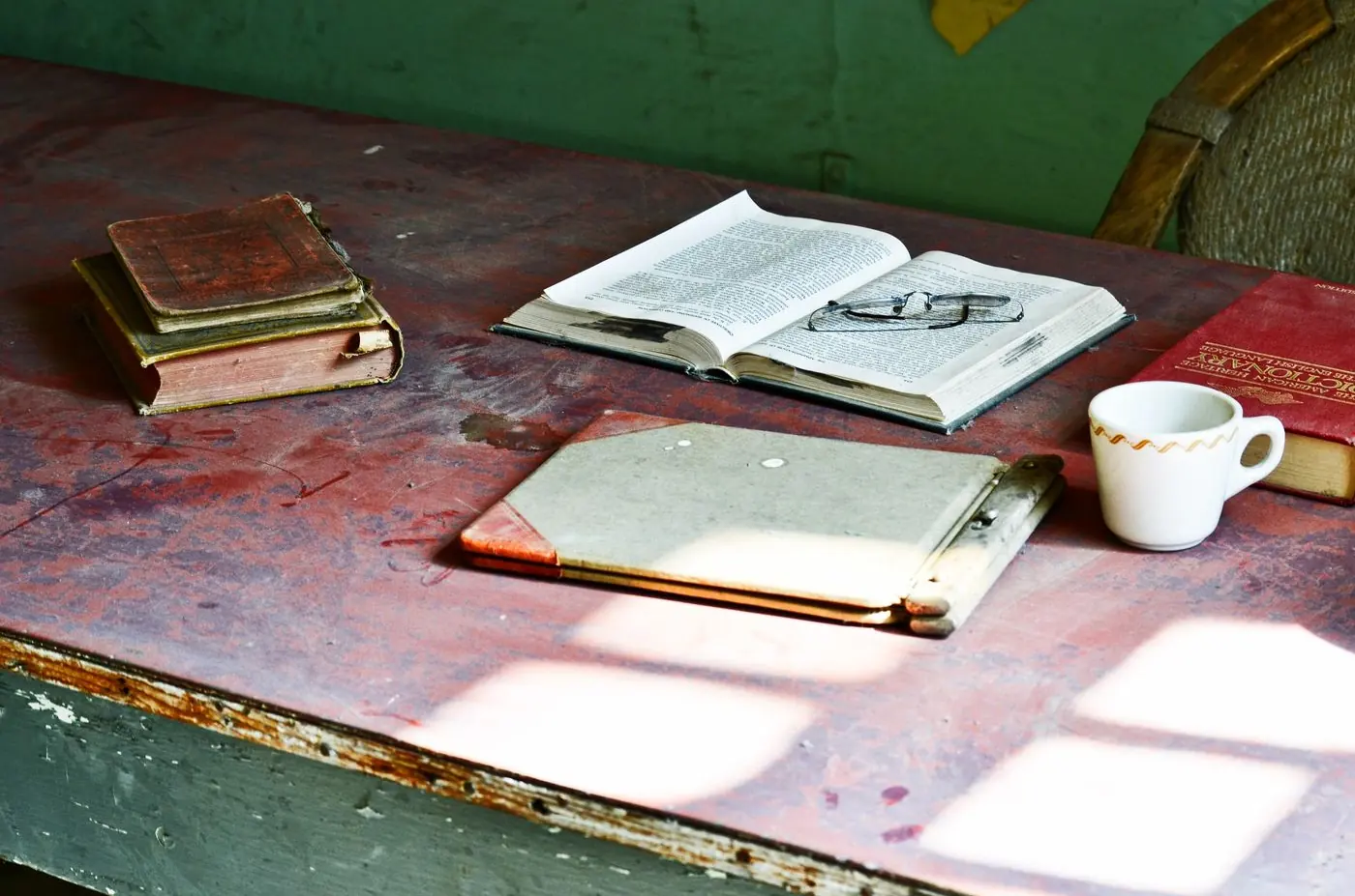 An open book and reading glasses on a desk in window light